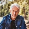 Portrait of a middle aged man with gray hair wearing a denim jacket outdoors with warm sunlight in the background