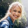 Smiling blonde woman wearing a denim jacket outdoors on a sunny day